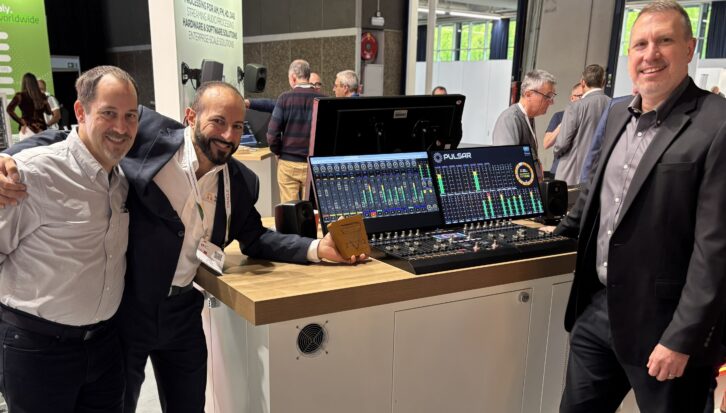 Three people in the Telos booth at IBC with a Pulsar console display