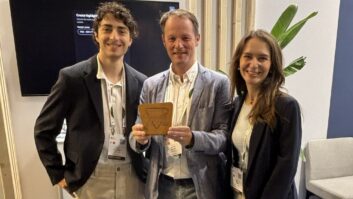 Three people stand in the deliver.media booth at IBC, one holding an award
