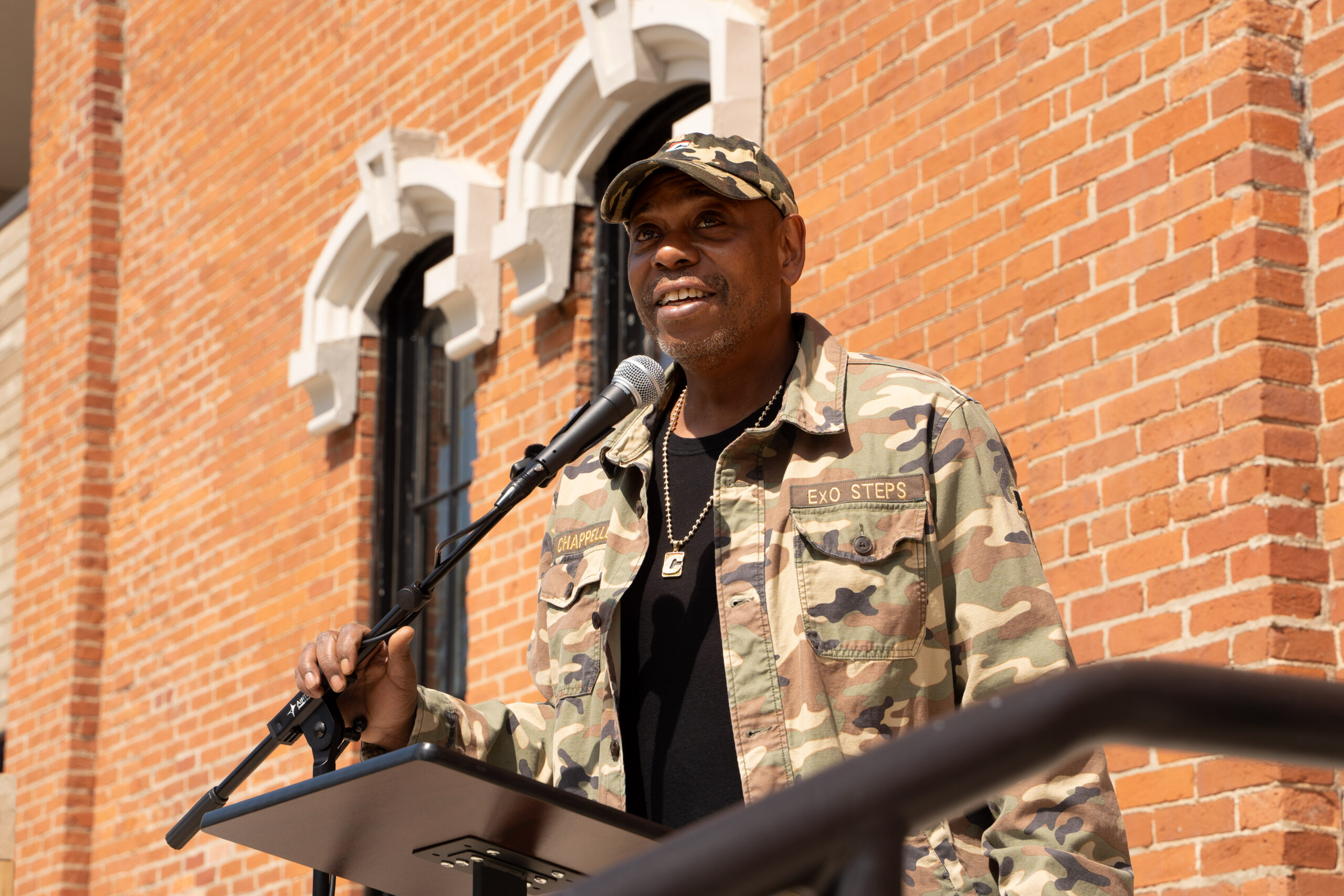 Luke Dennis stands at a podium and speaks into a microphone in front of Union Schoolhouse.