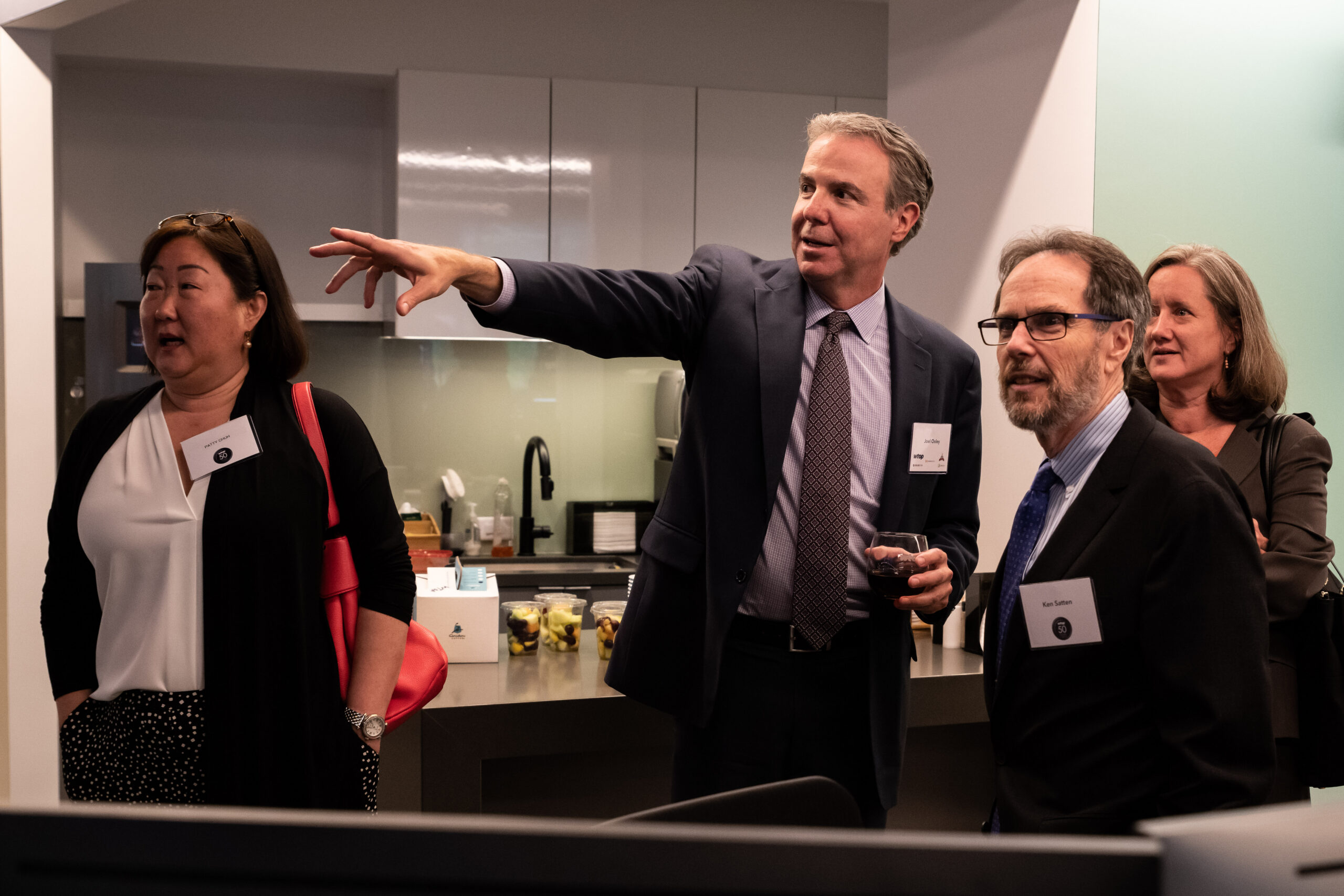 Joel Oxley, right, shows guests around WTOP’s new facilities in 2019. Walking behind him are Stanley Hubbard and Karen Hubbard. At work, seated center, is Zeke Hartner, and at lower right Jack Pointer. The station was also celebrating 50 years as an all-news outlet.