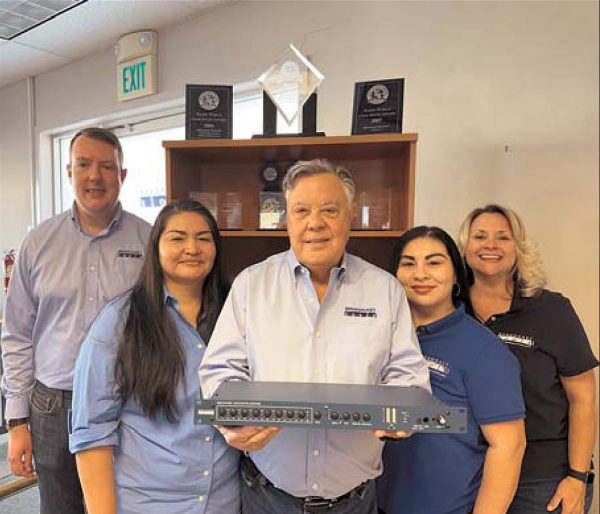 Five people stand in an office. The man in front holds a piece of broadcast equipment