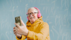 Senior man taking selfie with smartphone, listening music with headphones
