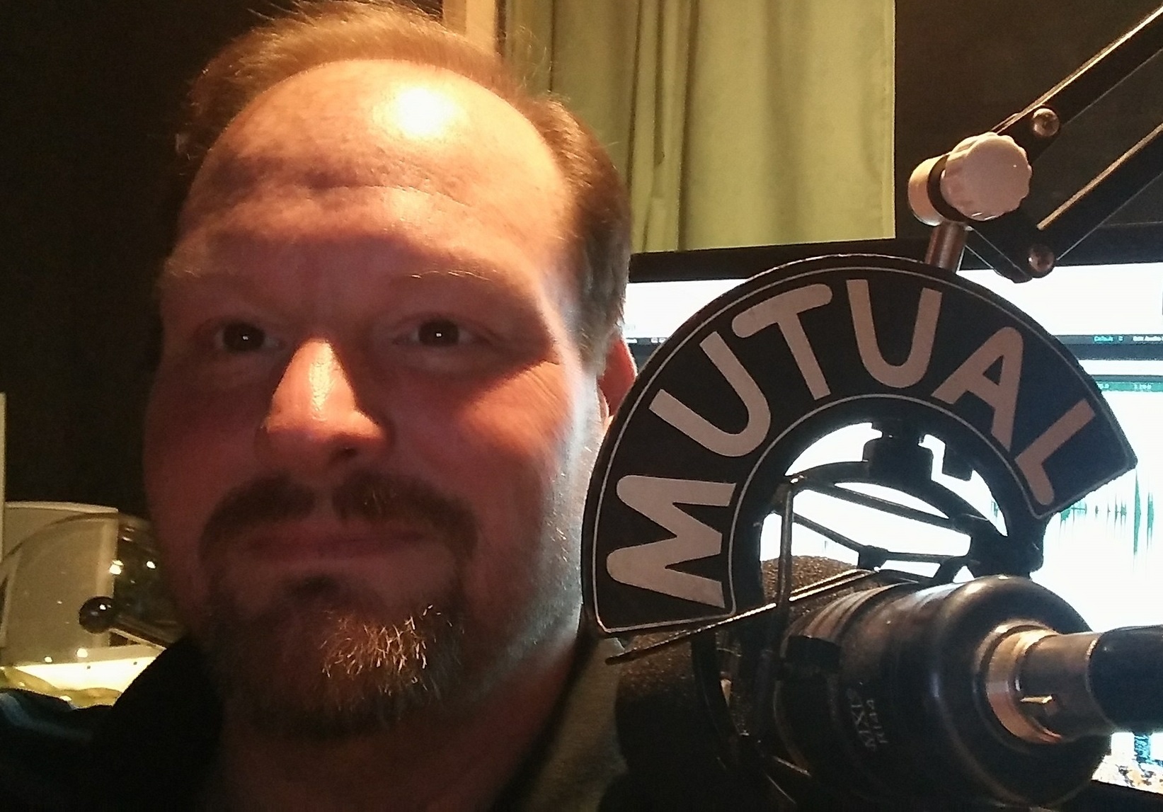 A photo of Leo Ashcraft sitting next to a microphone with a Mutual mic flag