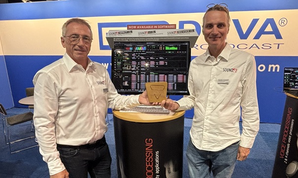 Two men stand in a booth at the IBC show with a computer screen and an award